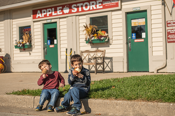 Two young boys eating apples in front of apple store.