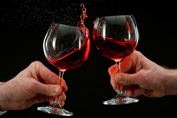 Two men clinking with glasses of red wine, celebrating success or speaking toast, close-up. Isolated on black background. Wine is splashing out of glasses.